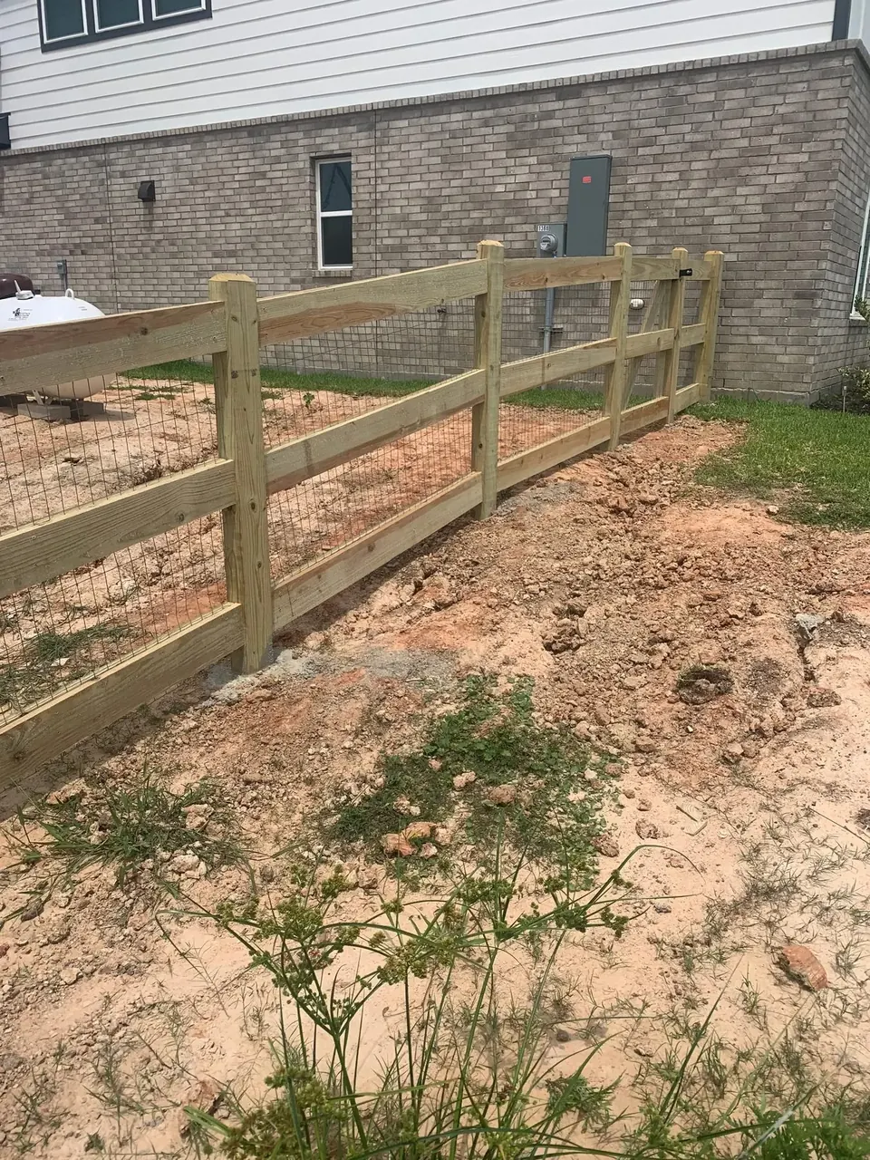 Wood ranch-style rail fence going up beside a home near Katy