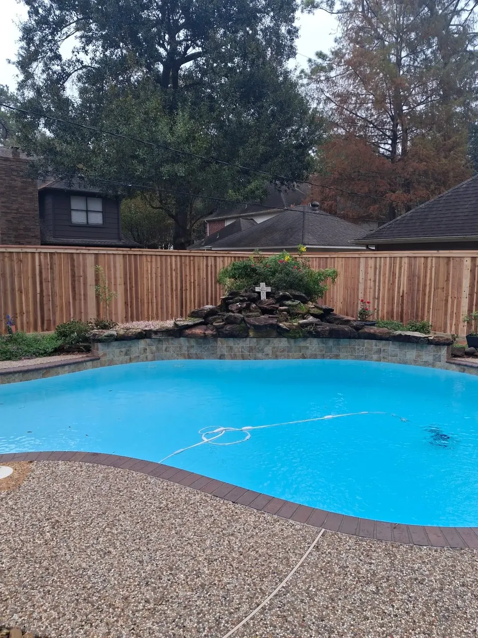 Cedar privacy fence behind a backyard pool and rock waterfall in Fulshear