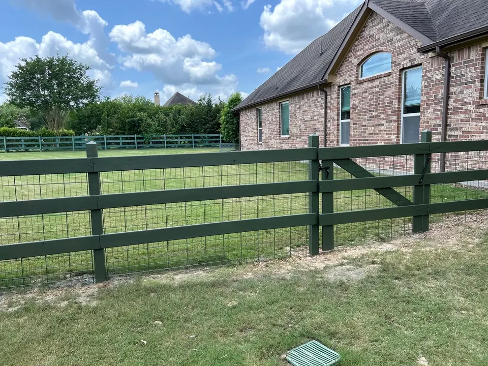 Green wood rail fence with wire mesh panels along the side of a Fulshear home