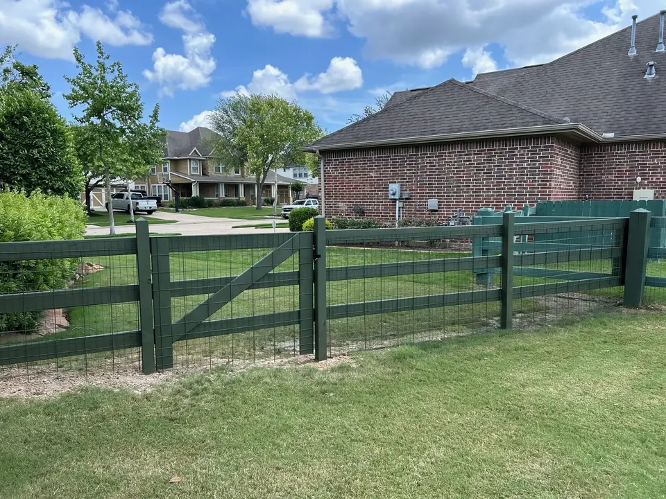 Green wood rail fence with wire mesh and a gate across a Fulshear front yard